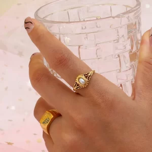 Gold vintage ring with pearl accent, worn on hand holding a clear glass.