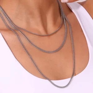 A model wearing a layered silver herringbone chain set, draping elegantly over her collarbone, styled with a white outfit.