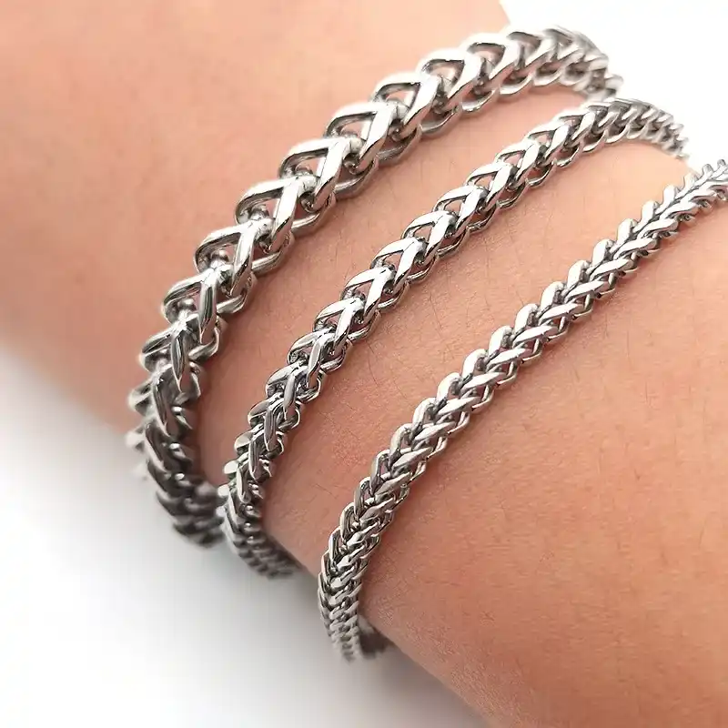Three stainless steel chain bracelets with different link styles worn on a wrist, featuring a polished silver-tone finish.
