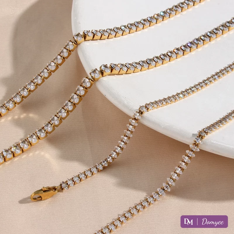 Two 18K gold jewelry sets: Left – thick chains with oval cubic zirconia stones; Right – thin chains with marquise-cut cubic zirconia, on white display stand and beige fabric