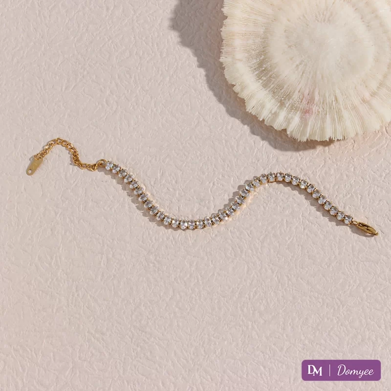 18K gold bracelet with cubic zirconia stones, elegantly displayed on a tabletop with a delicate shell, featuring a waterproof, fade-resistant, and hypoallergenic design.