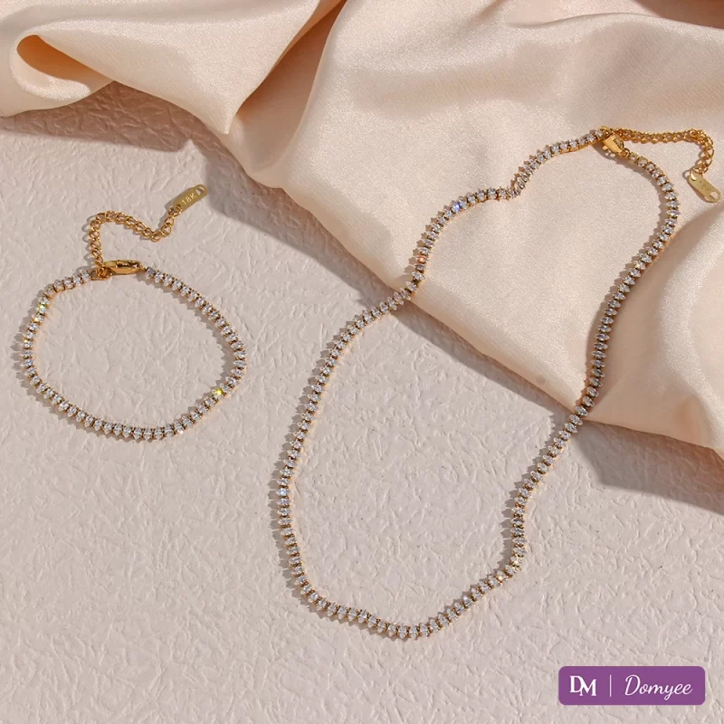 18K gold necklace and bracelet with marquise-cut cubic zirconia stones on a textured beige background, displayed with extended chains and adjustable clasps