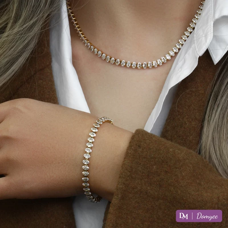 18K gold necklace and bracelet set with cubic zirconia stones, displayed on a woman’s neck and wrist against a white shirt and brown jacket