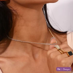 Woman’s neck and hand wearing 18K gold diamond necklace and three rings (black gemstone, pavé diamonds, gold band) against natural light