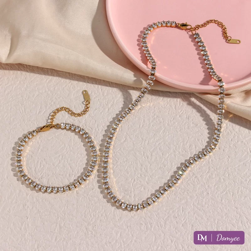 18K gold necklace and bracelet with oval-cut cubic zirconia stones on a light textured background, pink tray, and beige fabric