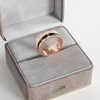 A rose gold-plated ring with a rotating band featuring Roman numerals, displayed in a gray velvet jewelry box, emphasizing its unique and elegant design.