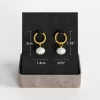 A pair of 18K gold-plated hoop earrings with white pearl drops, displayed on a black jewelry stand with size measurements indicated.